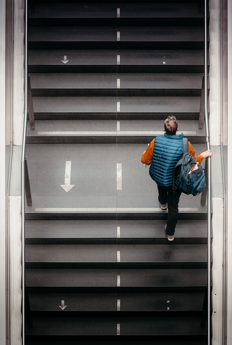 Man with backpack walks up escalator stairs