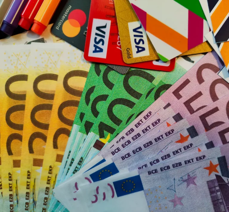 Gros plan sur des billets en euros de différentes coupures, des cartes bancaires Visa et Mastercard et des feutres de couleur disposés sur une table